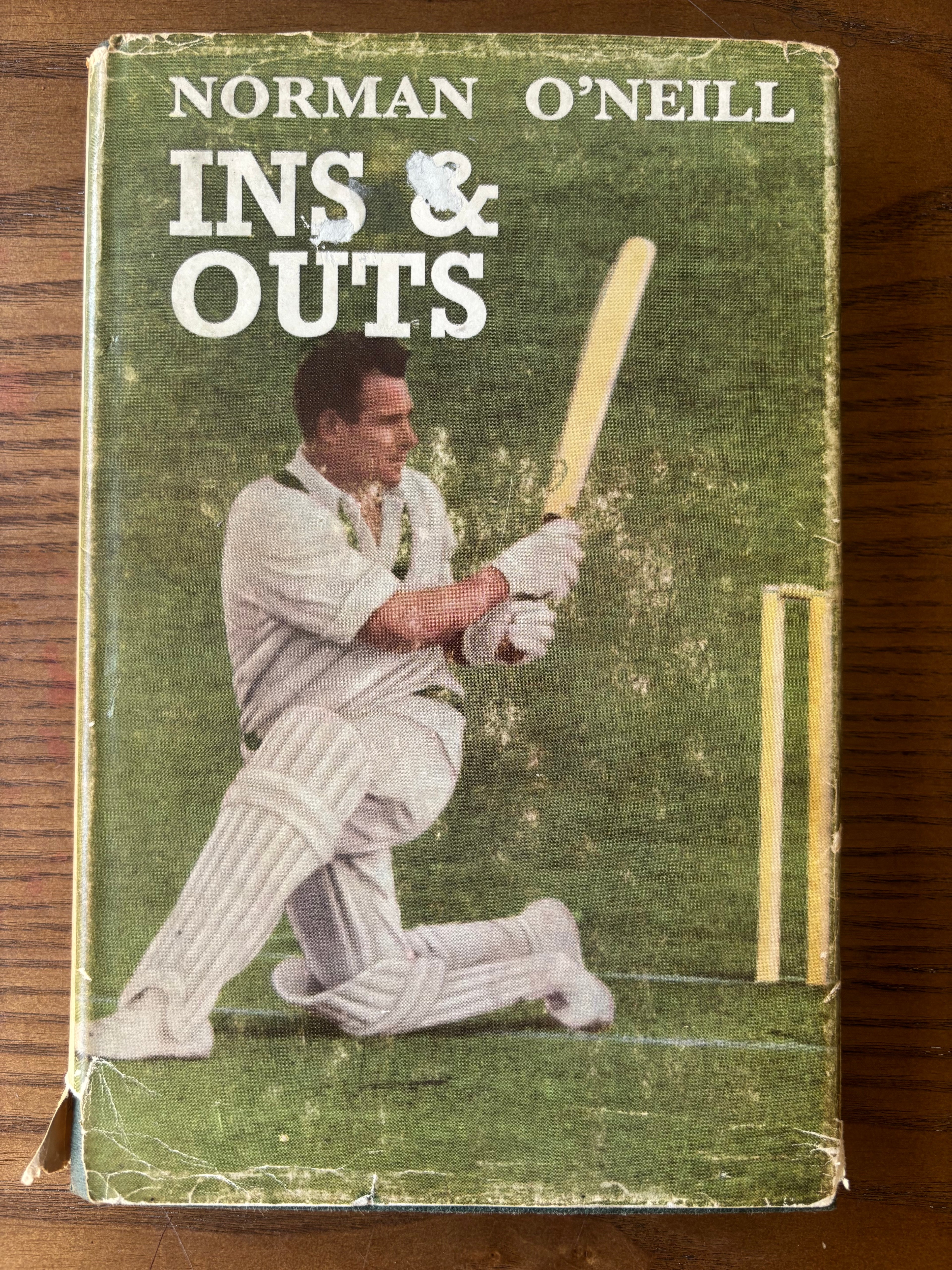 Vintage hardcover book of Norman O'Neill's 'Ins & Outs' featuring a cricket player on the cover, placed on a wooden surface.